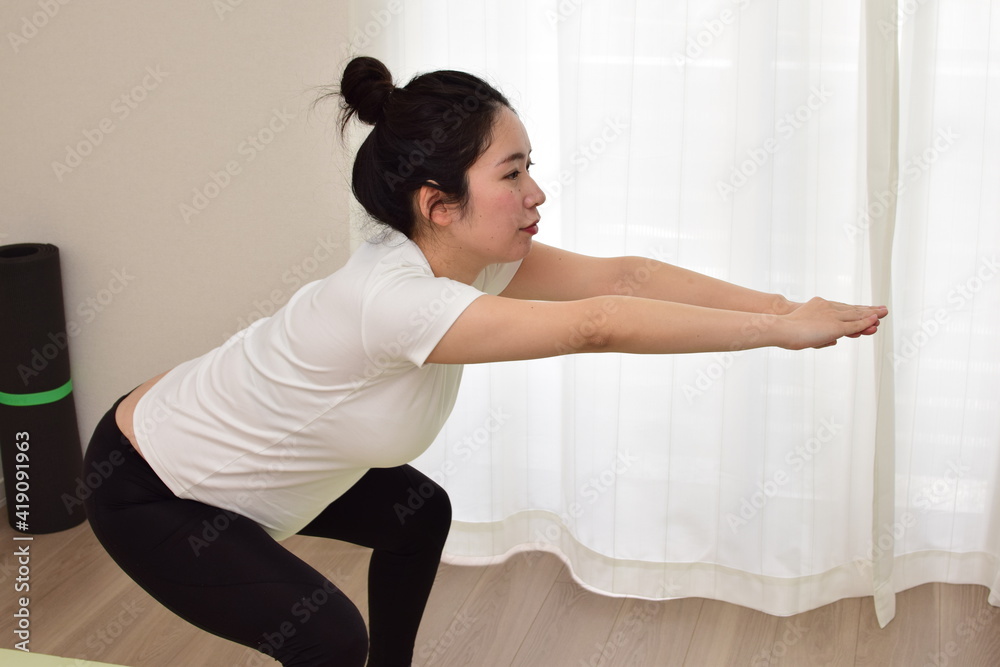 A young pregnant woman is doing fitness at home. She is squatting. It is important to exercise during pregnancy.