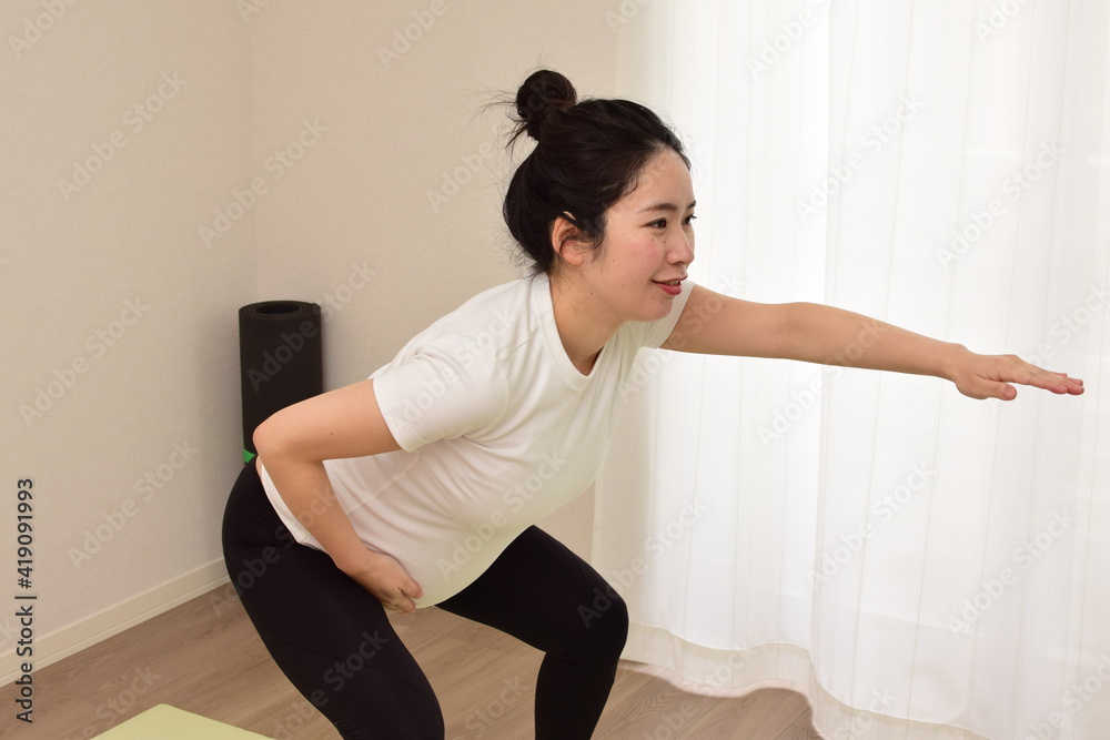 A young pregnant woman is doing fitness at home. She is squatting. It is important to exercise during pregnancy. A young pregnant woman is doing fitness at home. She is squatting. It is important to exercise during pregnancy.