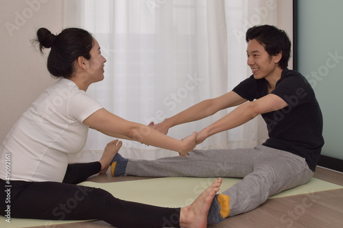 A young pregnant woman is doing fitness at home. My husband (partner) is helping me stretch. It is important to exercise during pregnancy.