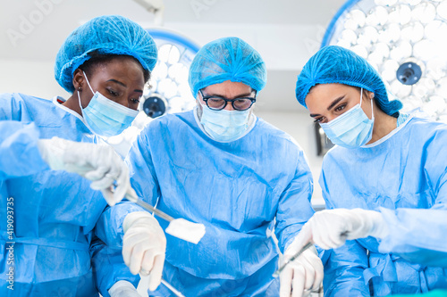 Portrait of team of multiethnic surgeons at work in a operation theatre. Several doctors surrounding patient on operation table during their work. Team surgeons at work in operating room.