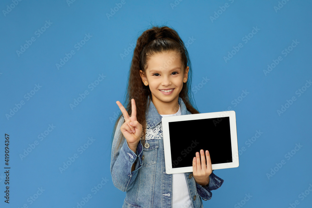pretty smiling little child girl shows empty tablet and Ok gesture on blue background pretty smiling little child girl shows empty tablet and Ok gesture on blue background