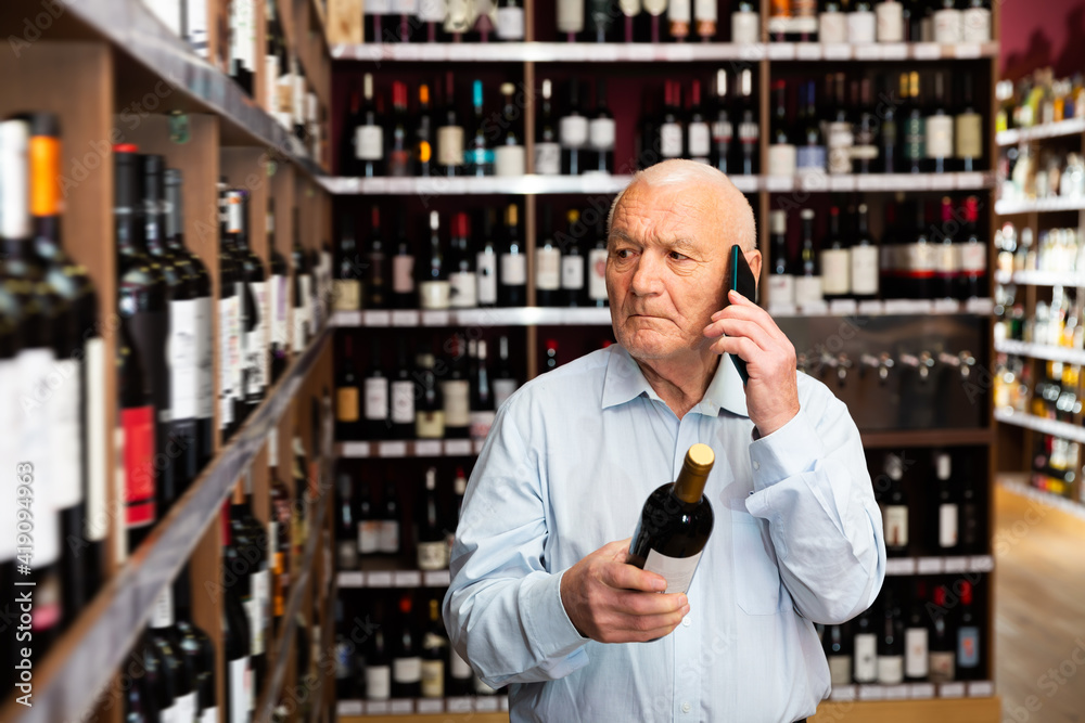 Serious man chooses wine and consults on a cell phone