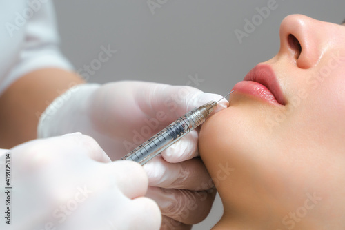 lip shape correction procedure in a cosmetology salon. The specialist makes an injection on the lips of the patient. Lip augmentation