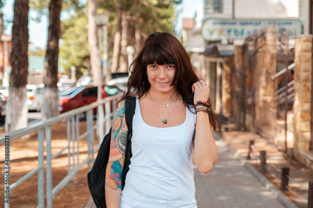 Summertime. Portrait of pretty woman with a tattoo on her arm, smiling and walking down the street. Concept of expression of emotions