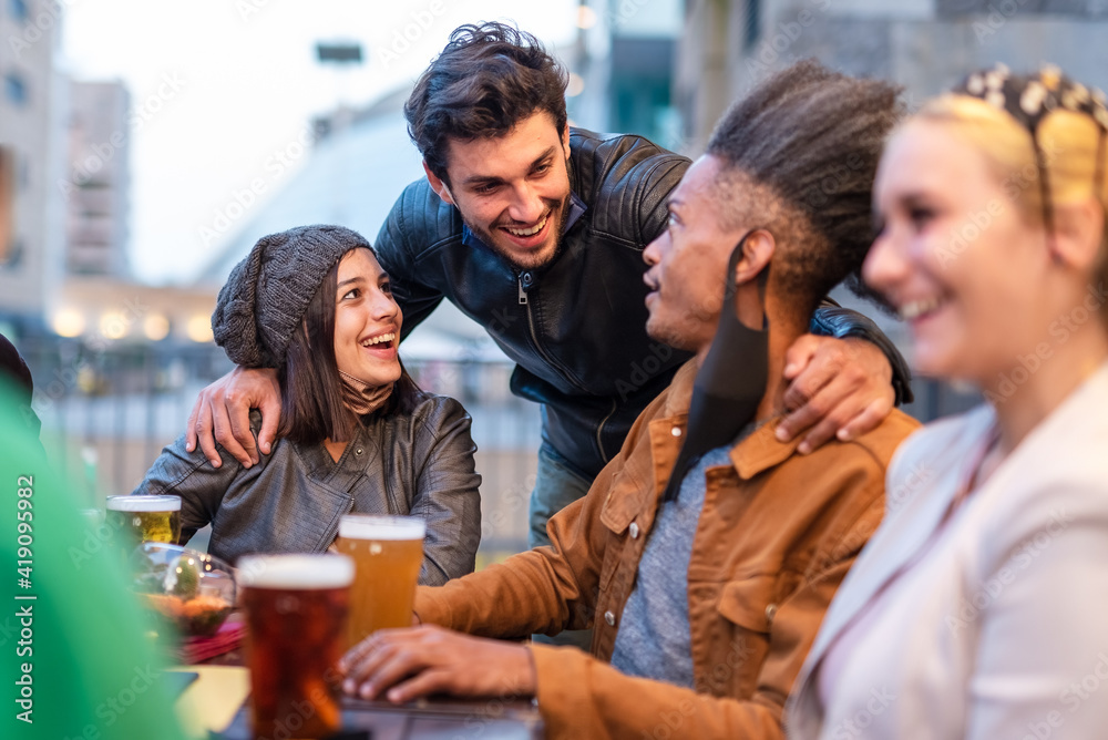 multi ethnic group of students chatting around a table in a brewery, gathering of young people during afternoon hours due curfew, restrictive health measures to prevent the spread of the corona virus