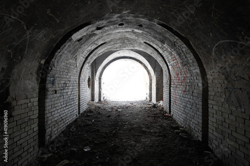 Exit from the old dark brick arched tunnel of the 19th century fortification. Light in the end of old abandoned tunnel.