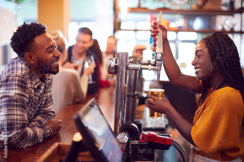 Smiling Female Bartender Behind Counter Serving Female Customer With Beer