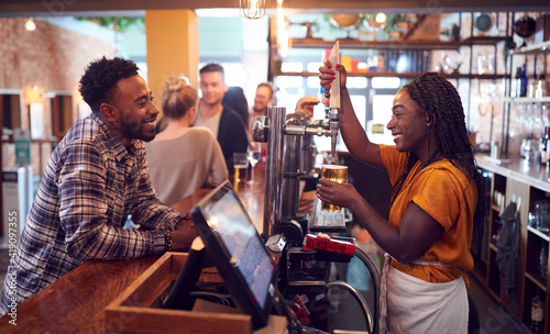 Smiling Female Bartender Behind Counter Serving Female Customer With Beer photo