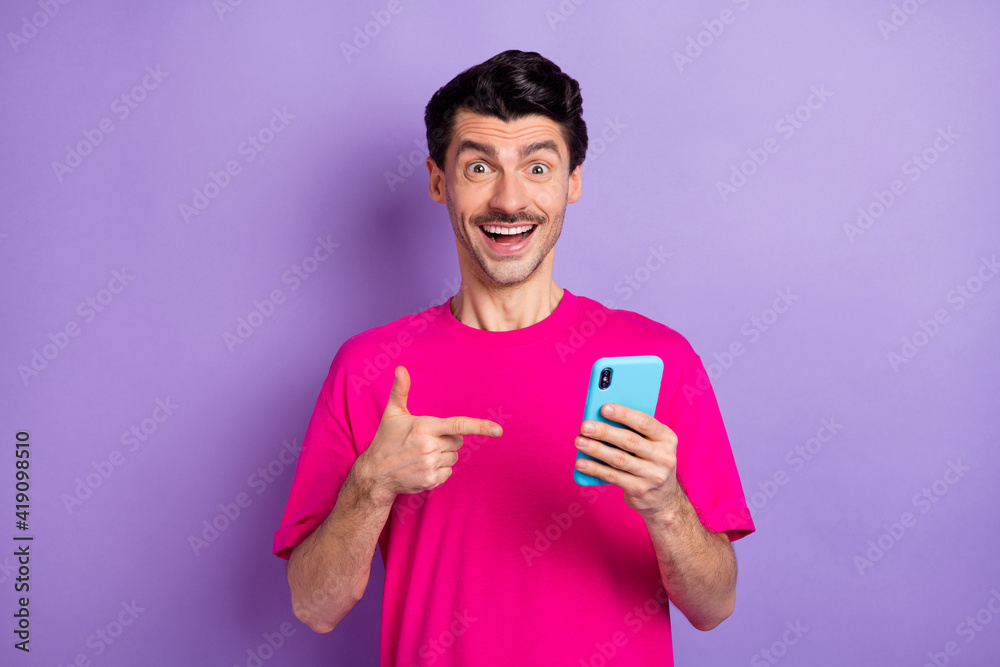 Photo of funky sweet young guy dressed pink t-shirt pointing finger modern device isolated violet color background Photo of funky sweet young guy dressed pink t-shirt pointing finger modern device isolated violet color background