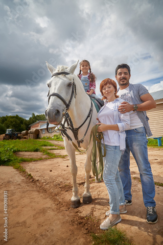 Kirov, Russia - August 07, 2020: A family including a mother, father and daughter walks and rides a horse in nature among green trees. Man, woman, girl with horse in nature in summer