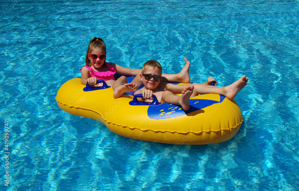 Boy and girl on inflatable float in outdoor swimming pool.