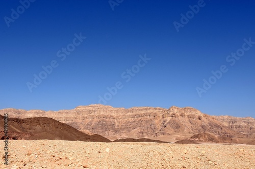 Desert landscape of Negev desert in Timna Park, Israel. The brownish colors and shades of rocks contrast with clear blue sky. There is a lot of copy space.