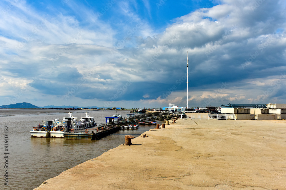 Coastal wharves with cumulonimbus clouds under blue sky and moorings for anchoring ships