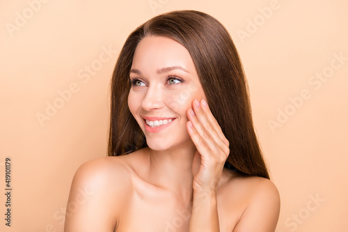 Photo of young girl happy positive smile hand touch cheek perfect pure skin look empty space isolated over beige color background