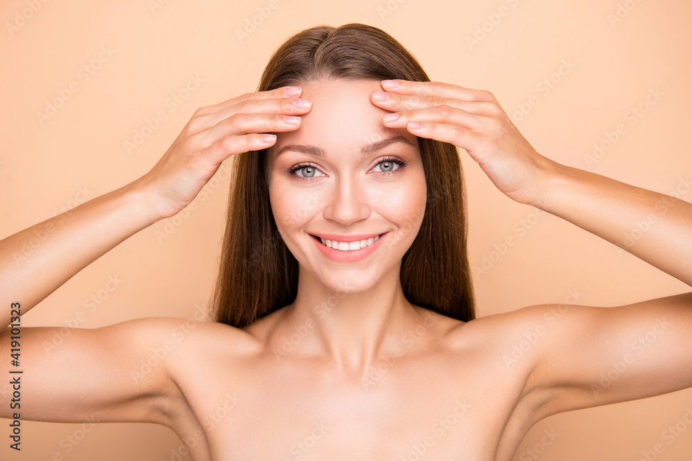 Photo of young girl happy positive smile hands touch forehead cleansing skin isolated over beige color background Photo of young girl happy positive smile hands touch forehead cleansing skin isolated over beige color background