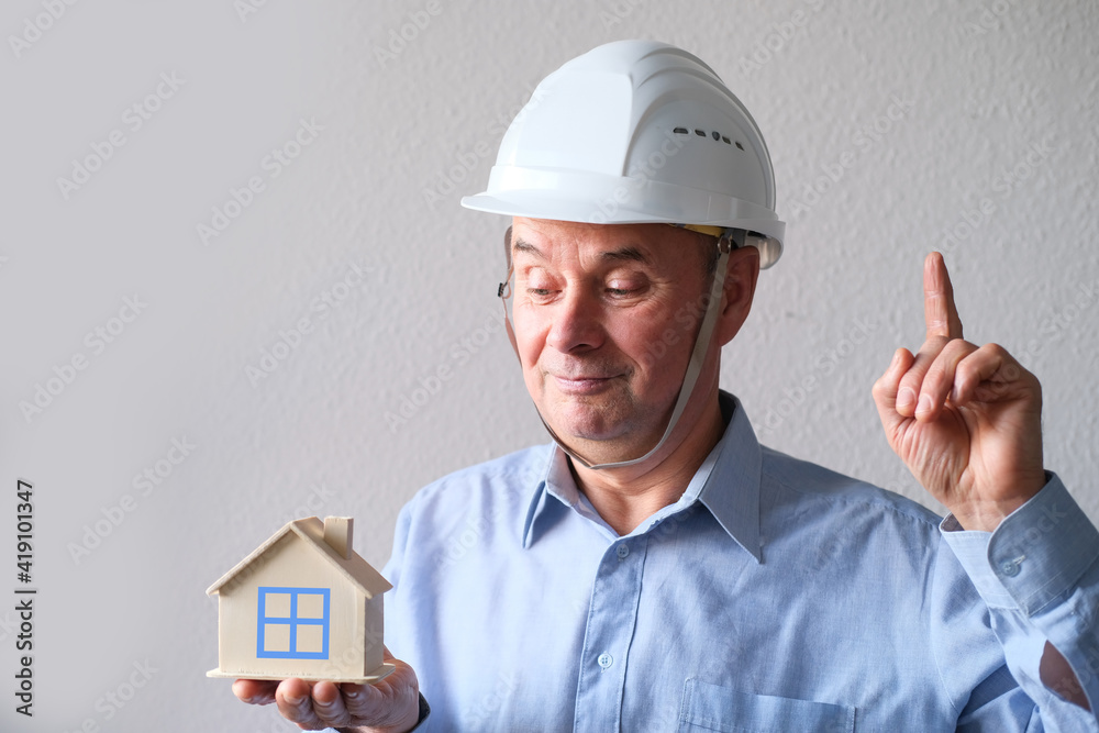 elderly male agent, a builder in a protective helmet, glasses offers to rent, buy a house, shows a model of a house, a mortgage concept, advice on buying a property elderly male agent, a builder in a protective helmet, glasses offers to rent, buy a house, shows a model of a house, a mortgage concept, advice on buying a property