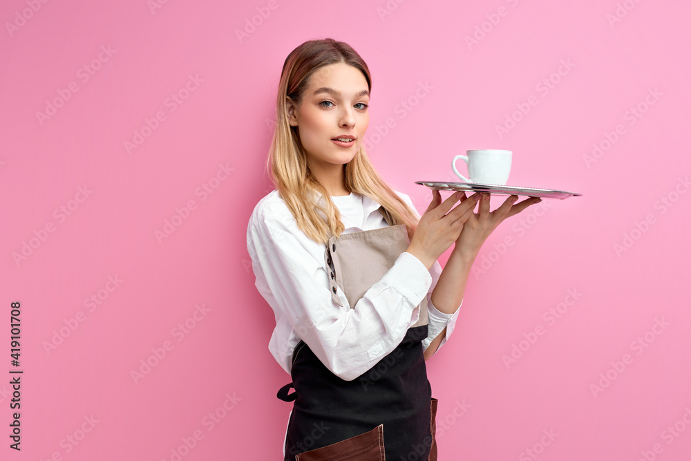 nice woman waitress in apron, offering cup of delicious tasty coffee, stand looking at camera, friendly staff of cafe restaurant. isolated over pink studio background nice woman waitress in apron, offering cup of delicious tasty coffee, stand looking at camera, friendly staff of cafe restaurant. isolated over pink studio background