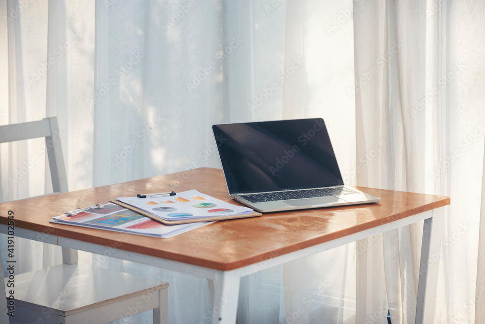 Fototapeta premium Office laptop business financial document chart and graph on wooden table with coffee cup. Flat lay notebook computer laptop on office desk. No people business graph chart mockup on business workspace