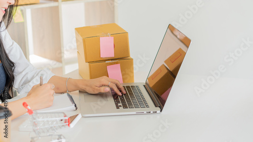 Small Business Startup Freelance SME Entrepreneurs Beautiful Asian Young Women Working at Home with Box, Smartphone, Laptop on the Table with Online Sales, Marketing, Packaging, SME Shipping, Ecommerc photo