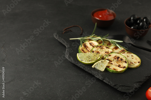 Delicious grilled zucchini slices served with lime and rosemary on black table. Space for text