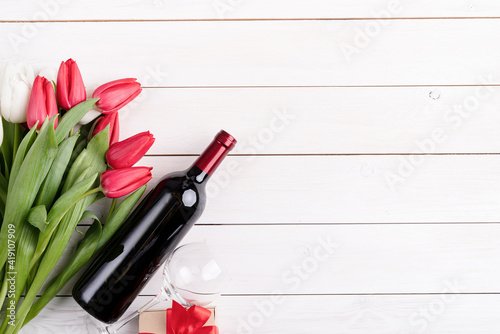 Bunch of colorful tulips and wine bottle on white wooden background