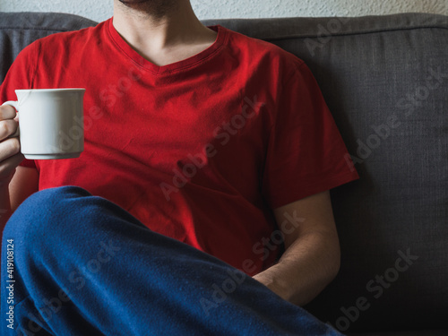 Person in red t-shirt drinking a cup of coffee on the sofa photo