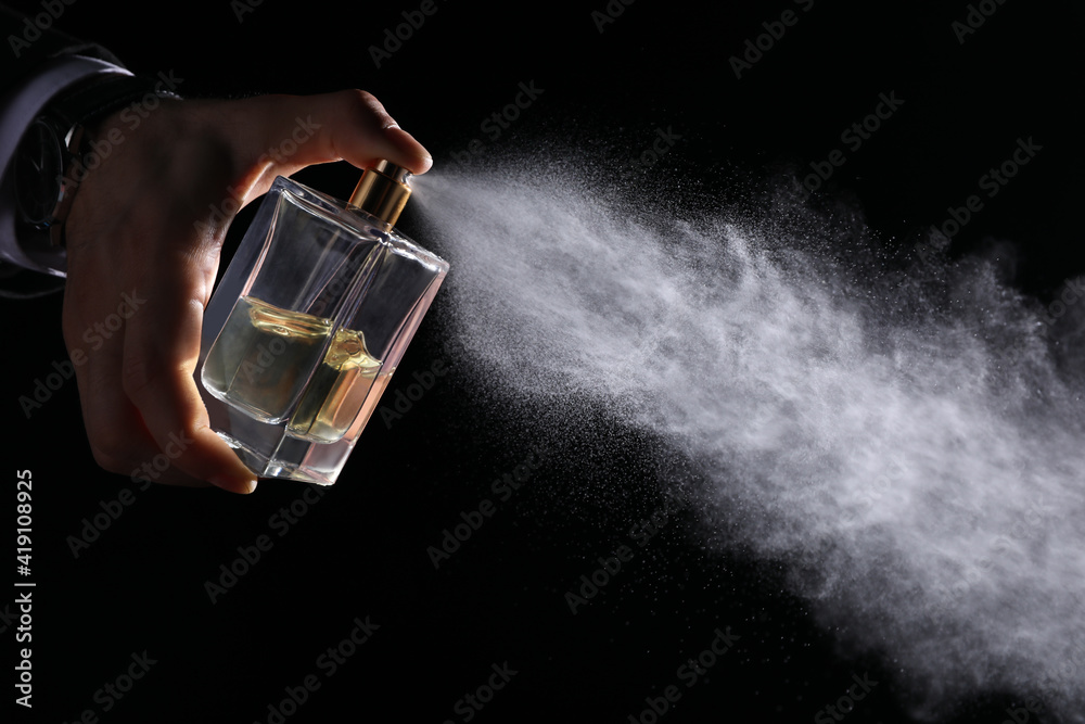 Man spraying luxury perfume on black background, closeup