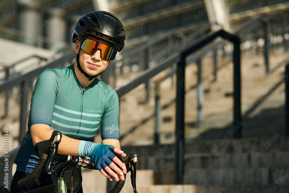 Portrait of professional female cyclist in cycling garment and protective gear posing for camera while having a training, riding bicycle in city center Portrait of professional female cyclist in cycling garment and protective gear posing for camera while having a training, riding bicycle in city center