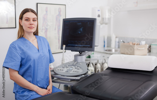 Female sonographer sitting near ultrasound machine in clinic smiling confidently