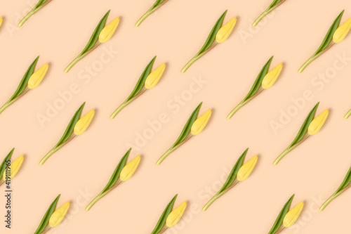 Repetitive pattern made of yellow tulip flowers on a beige background. Creative art concept.