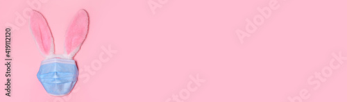 Pink bunny rabbit with face protective mask on pink background. Easter quarantine concept.Copy space for text, top view, flat lay. Banner