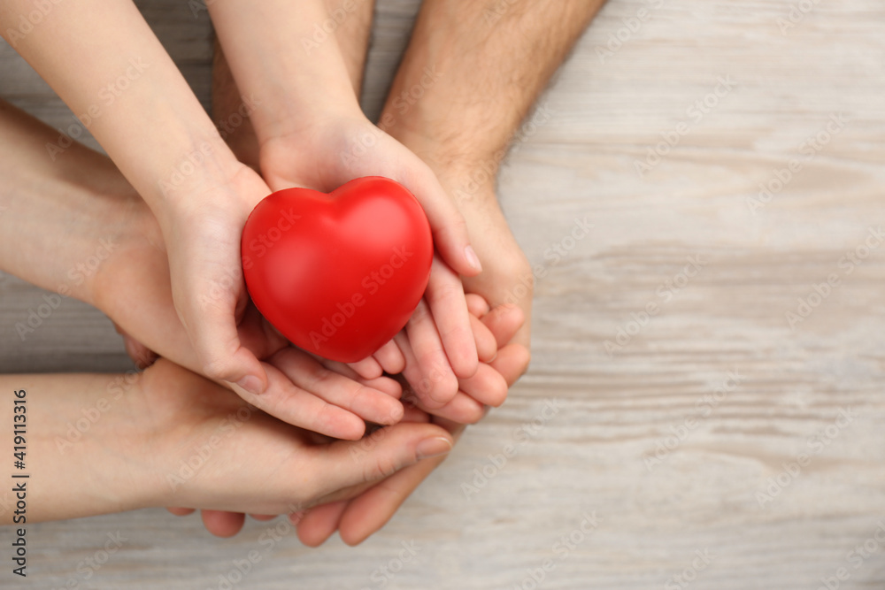 Top view of parents and kid holding red heart in hands at wooden table, space for text. Family day