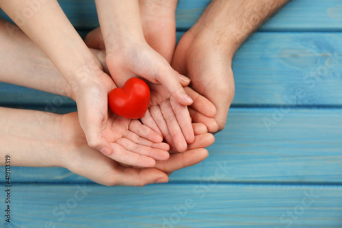 Parents and kid holding red heart in hands at turquoise wooden table, top view. Family day