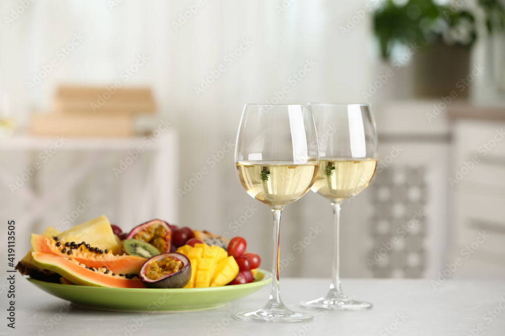 Delicious exotic fruits and glasses of wine on white table indoors