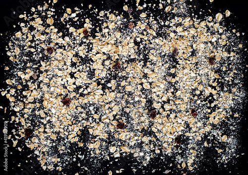 top view of oat flakes scattered on a black background, a pattern of instant oatmeal, healthy breakfast, precooked porridge with freeze-dried berries