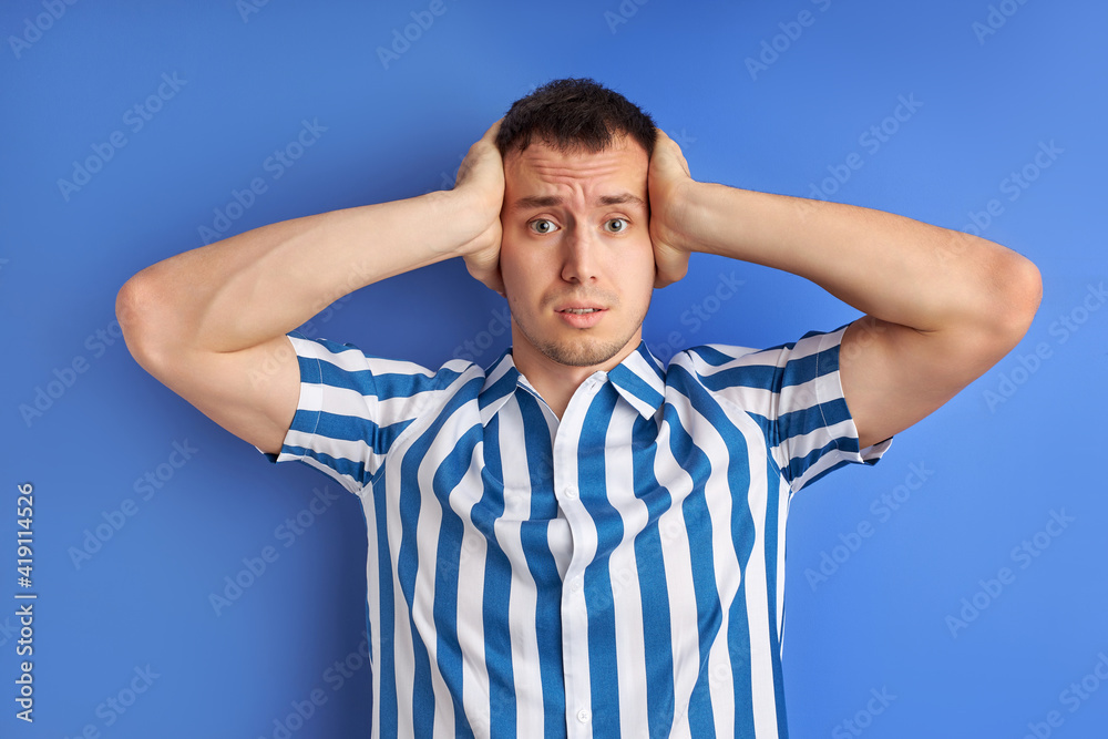 Annoyed young caucasian man plugging ears with hands. Portrait of young man, student, worker, employee covering his ears from loud noise, having headache isolated on blue background Annoyed young caucasian man plugging ears with hands. Portrait of young man, student, worker, employee covering his ears from loud noise, having headache isolated on blue background