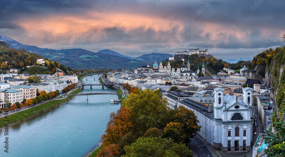 Fototapeta premium Aerial panoramic view of the famous historic city of Salzburg with Hohensalzburg Fortress and Salzach river with colorful sky during sunset. Popular travel and historical center of Austria.