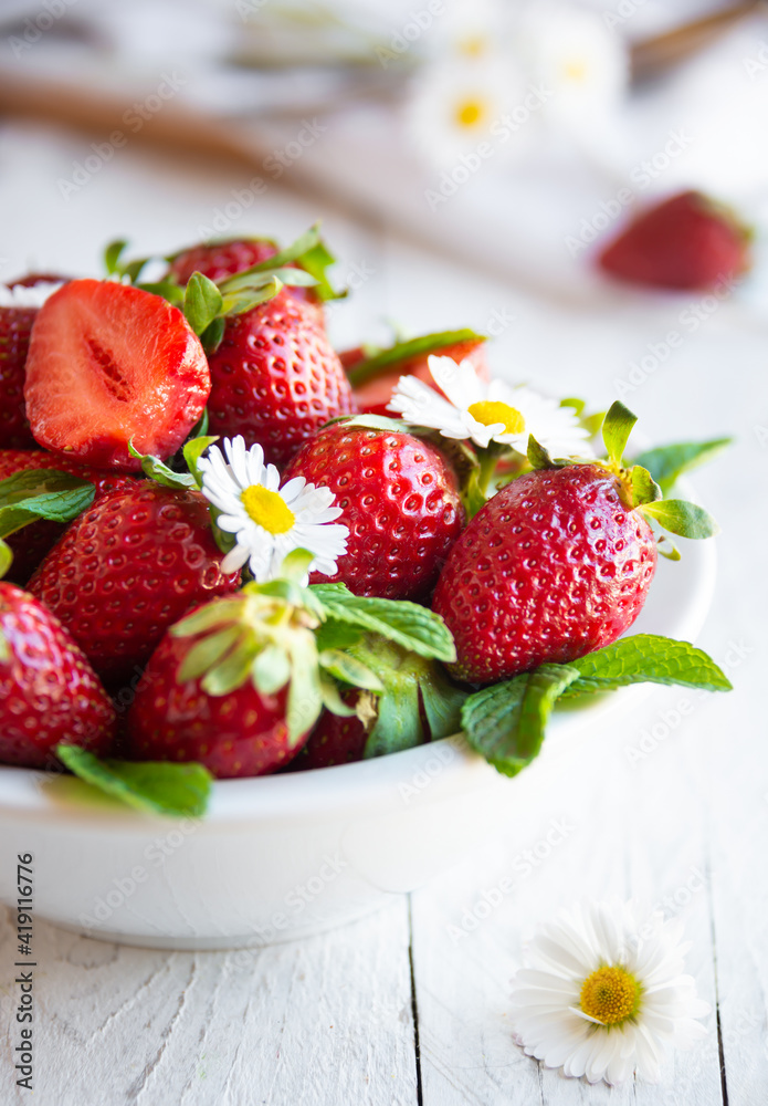 Fresh strawberries in white bowl with leaves and flowers Fresh strawberries in white bowl with leaves and flowers