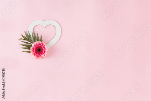 Love concept with copy space, pink daisy and green leaves, on a pink background. Minimal flower flat lay.