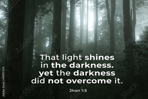 Bible inspirational words - That light shines in the darkness, yet the darkness did not overcome it. Bible verse Jhon 1:5 On background of misty forest with natural light in the dark. photo