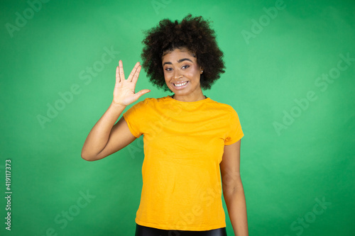 African american woman wearing orange casual shirt over green background doing star trek freak symbol