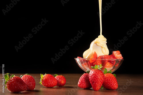 Strawberries, crystal bowl with strawberries and condensed milk on a table, black background, selective focus. photo