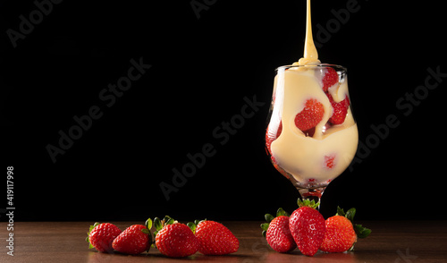 Fotografía Strawberries, crystal bowl with strawberries and condensed milk on a table, black background, selective focus