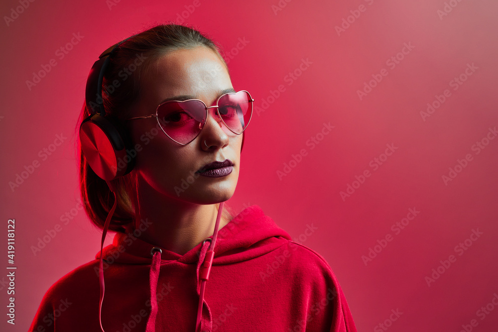 Fashion hipster woman wear stylish glasses and headphones listening to music over color neon background at studio. Fashion hipster woman wear stylish glasses and headphones listening to music over color neon background at studio.