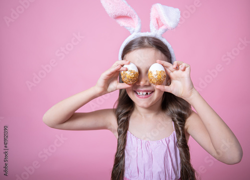 A funny little girl dressed in Easter bunny ears and in a dress posing with Easter eggs copy space.