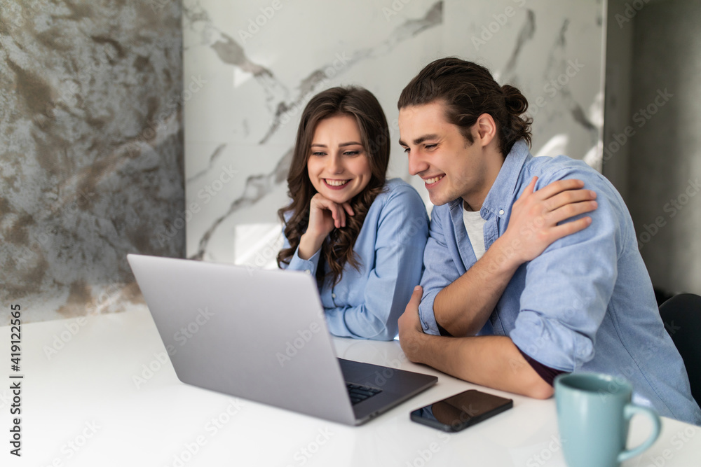 Beautiful young couple is using a laptop and smiling while having a breakfast at home Beautiful young couple is using a laptop and smiling while having a breakfast at home