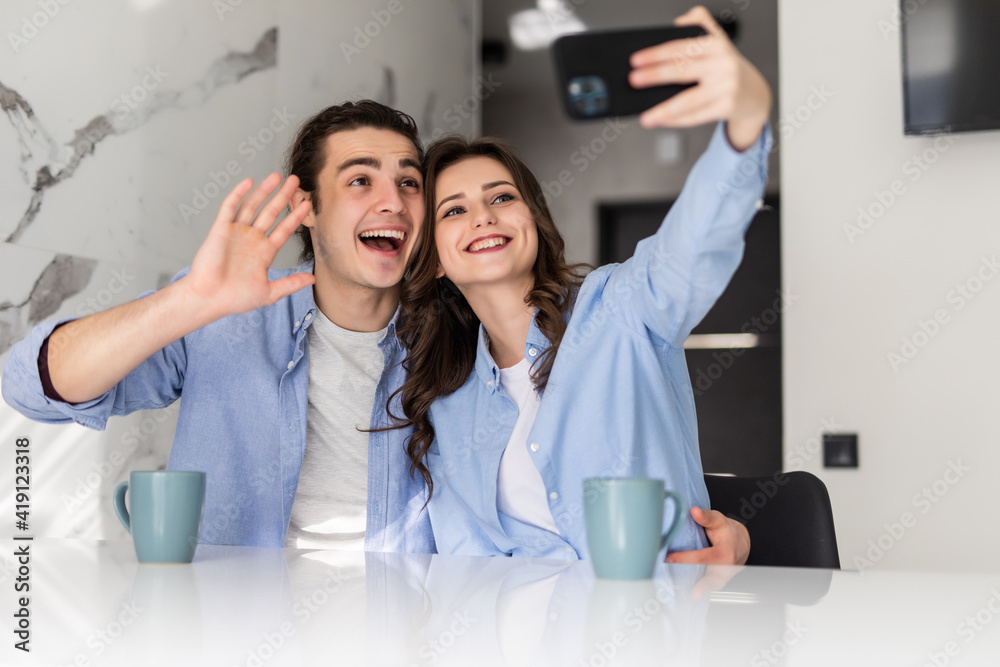 Young couple taking a selfie while sitting at the kitchen