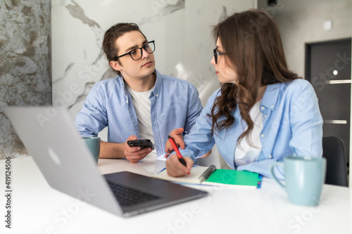 Happy young husband and wife using laptop looking at screen pay bills online in app calculate mortgage investment payment on website, planning budget, discuss finances sit at home table
