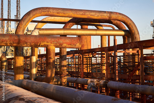 Tangle of gas collector steel pipes rust covered with traces of corrosion and aging. Concept of complexity of petrochemical industry communications. Various diameters pipe weaving valves and flanges photo