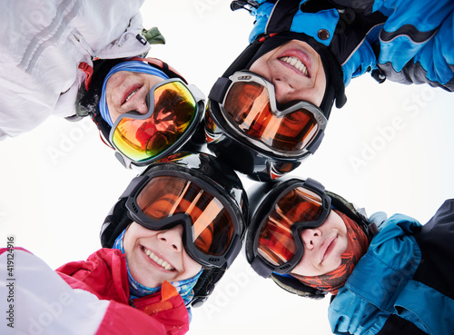 Close up of happy friends skiers in ski glasses touching heads and expressing positive emotions. Group of joyful people wearing ski helmets and goggles. Concept of friendship and skiing.